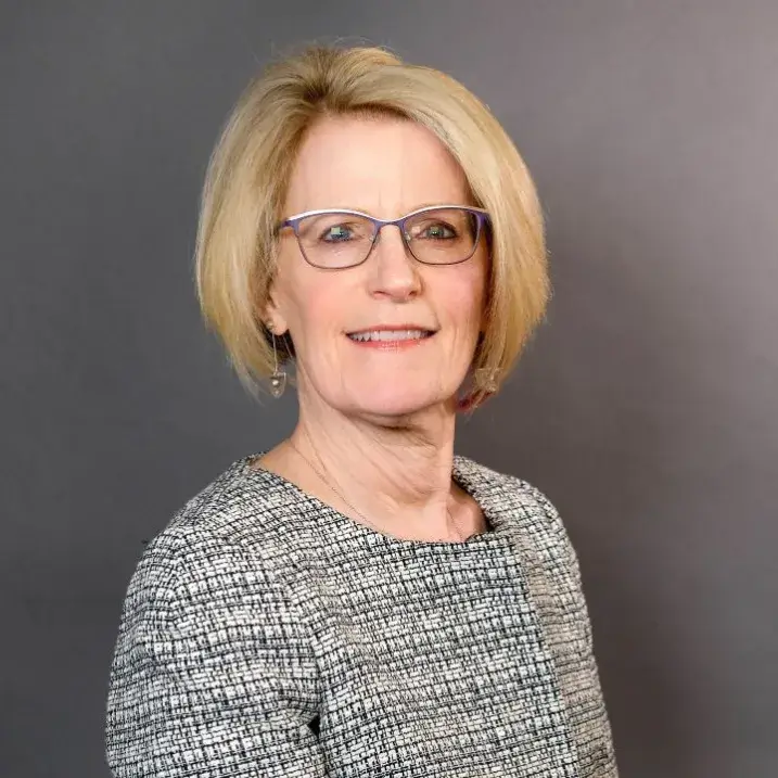 Portrait of a woman with blond hair, wearing glasses, and a black and silver blouse
