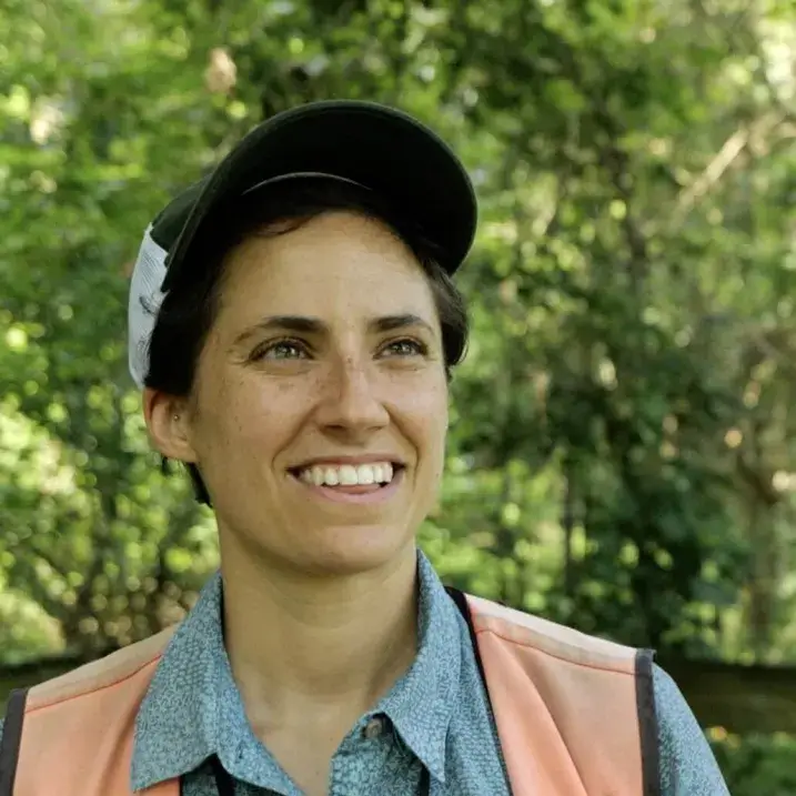 Grace wearing an orange work vest in the woods