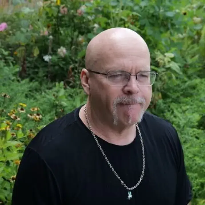 Brian in a black t-shirt in front of flowers