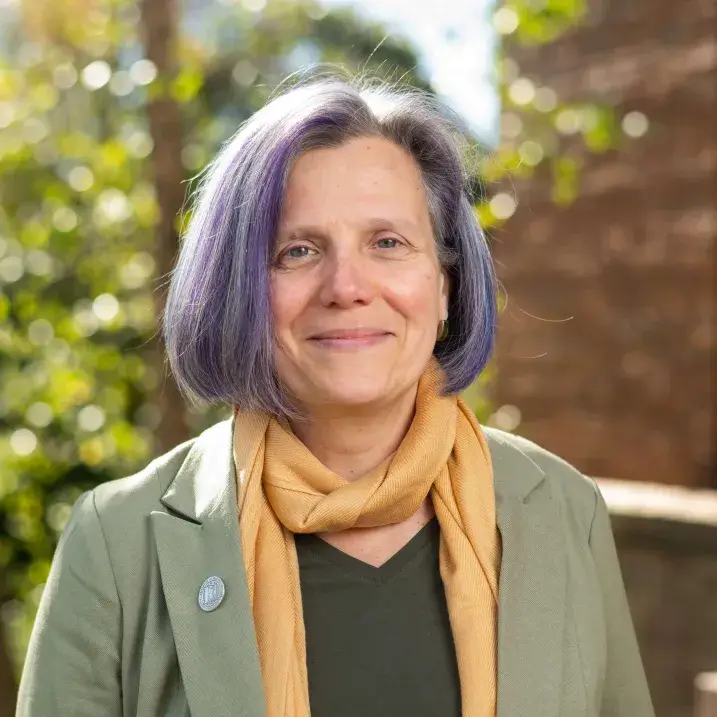 Image of Darcy with trees and brick building in the background