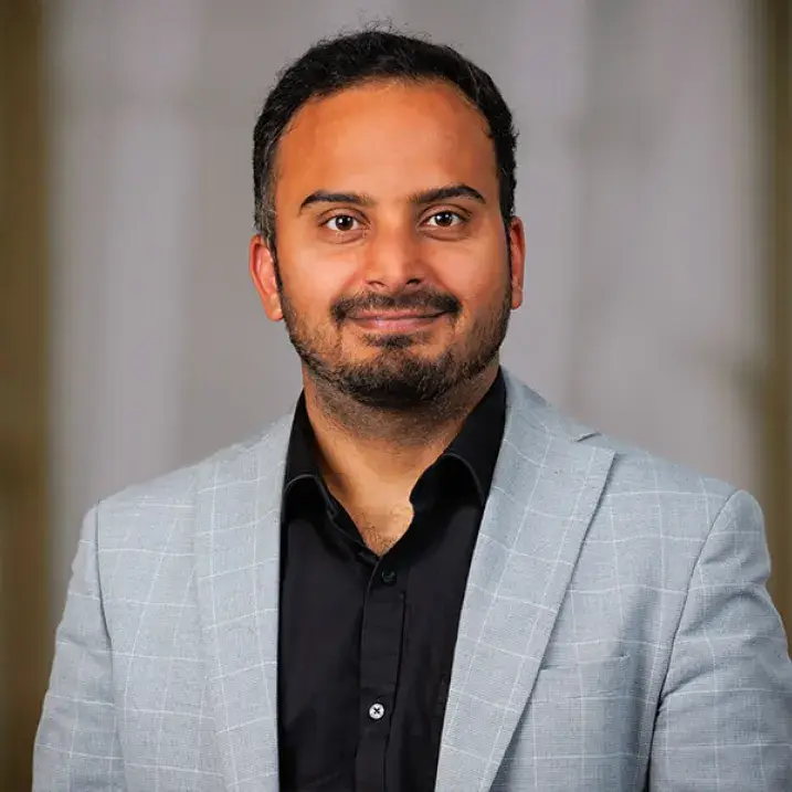 A man in a black shirt and gray blazer with short hair looks at the camera for a headshot.