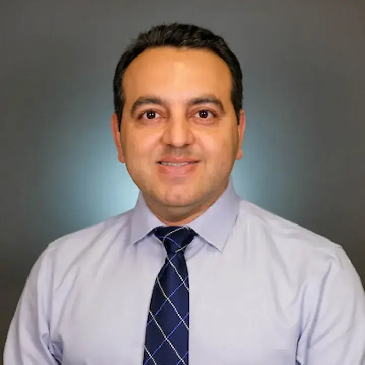 Headshot of an individual with black hair, wearing a grey shirt with a striped navy blue tie