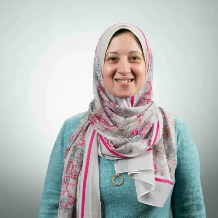 Person in pink and white head scarf and turquoise sweater.