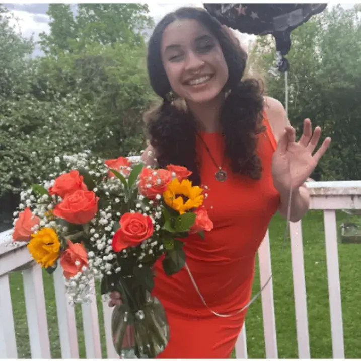 Lexie-Anne Madden wearing a orange dress, smiling and holding flowers in her left hand and a balloon in her right hand
