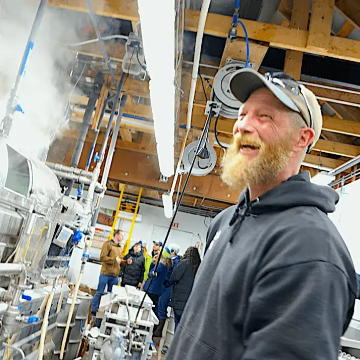 bearded, laughing Wade in ballcap in front of steaming evaporator