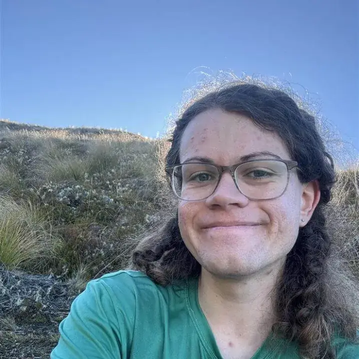 Pale-skinned woman in their mid-twenties with glasses and wavy brown hair pulled back behind their ears