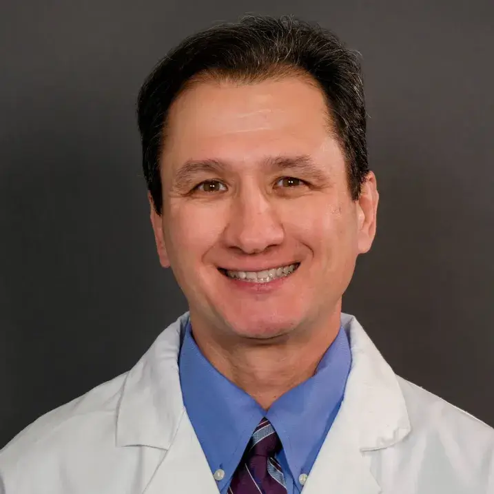 person with short brown hair, blue shirt and tie and a white doctors coat