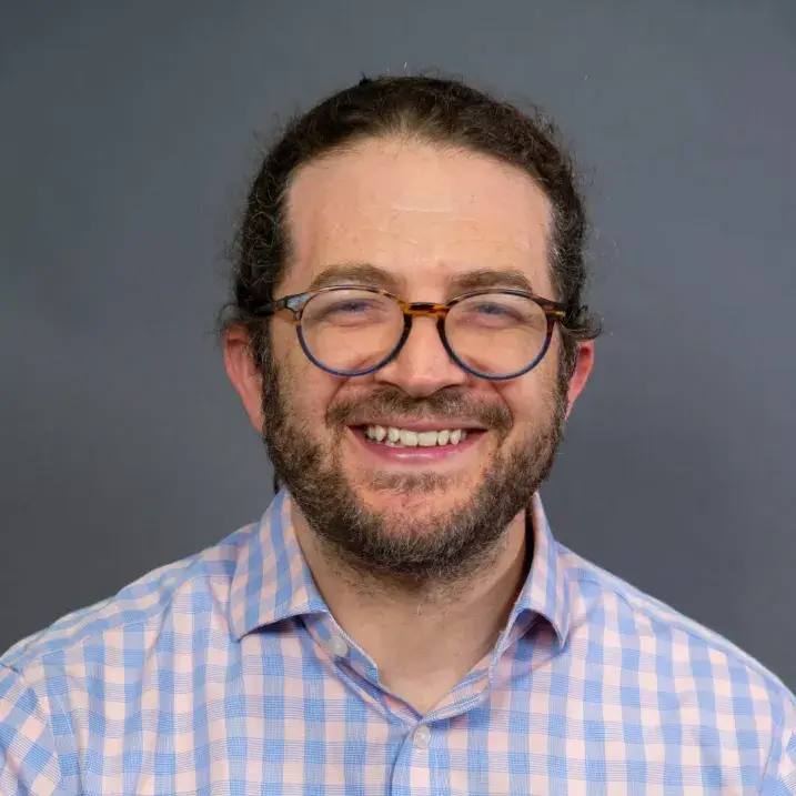 person with a heavy beard and moustache, brown rimmed glasses and blue and white gingham dress shirt