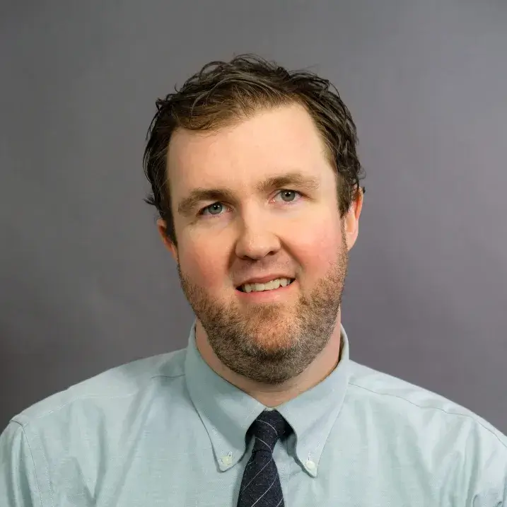 man with light skin, short brown hair and light beard wearing a light green shirt and dark tie