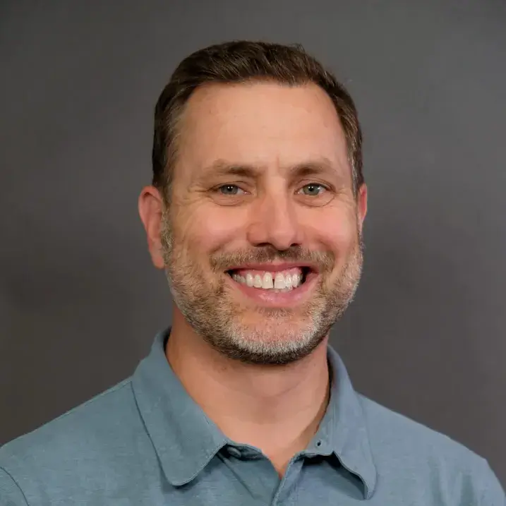 man in a blue button up shirt with light beard and short brown hair