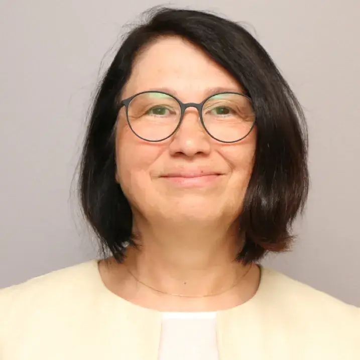 Woman wearing dark rimmed glasses with black hair smiling and wearing a yellow blazer over a white blouse.
