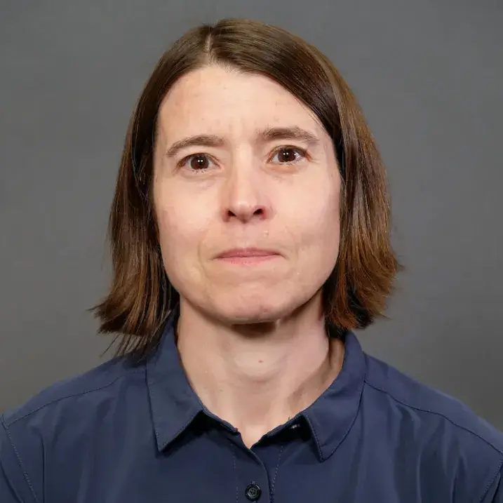 Woman with auburn hair wearing a dark blue button downed shirt.