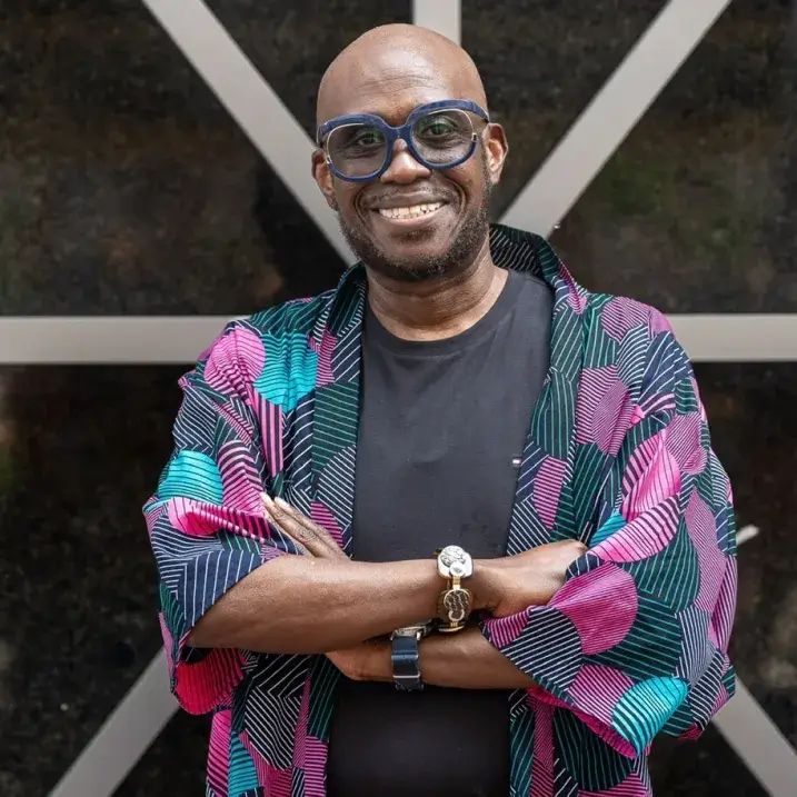 Rev. James standing in front of a wall, wearing a multi color cardigan with his arms crossed in front of him 