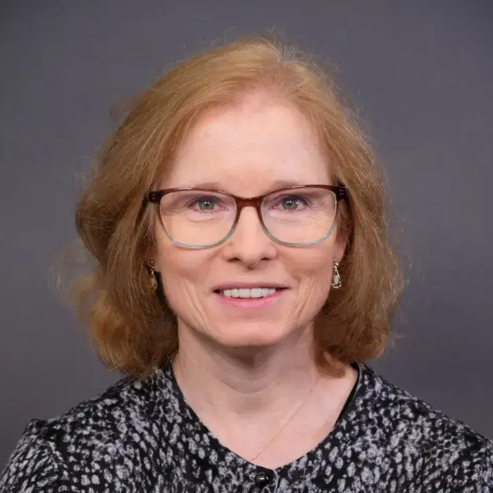light skinned woman with glasses, long auburn hair and a patterned top