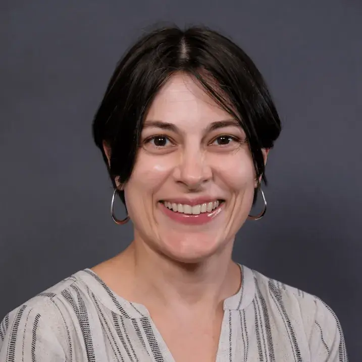 Black haired woman smiling, wearing large silver hoop earrings and an off-white and black striped linen blouse.  
