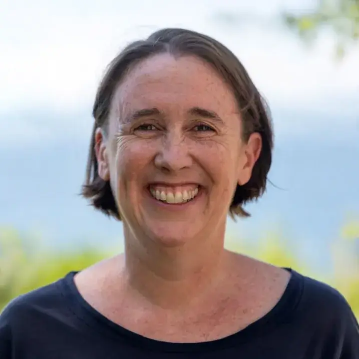 Woman with short straight brown hair and freckles, smiling and wearing an oval cut navy blue blouse. 