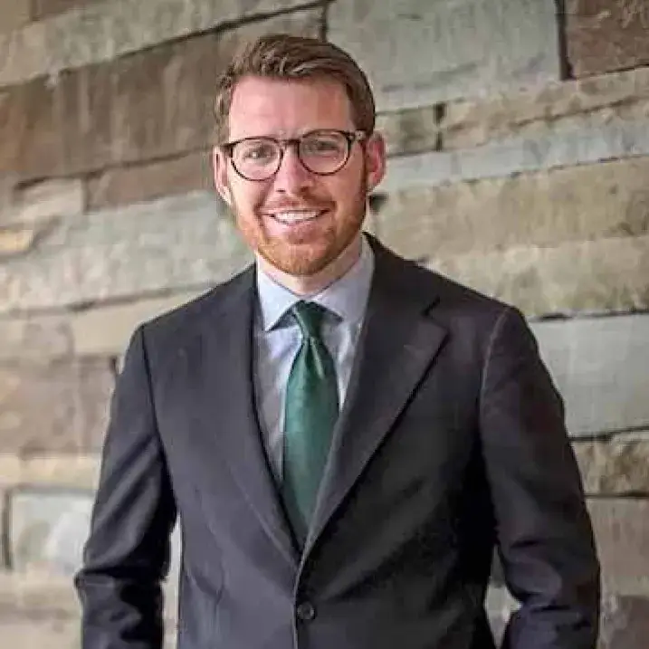 man with beard and glasses wearing a gray jacket and green tie