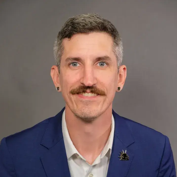 light skinned man with short gray hair wearing a white shirt and navy blazer