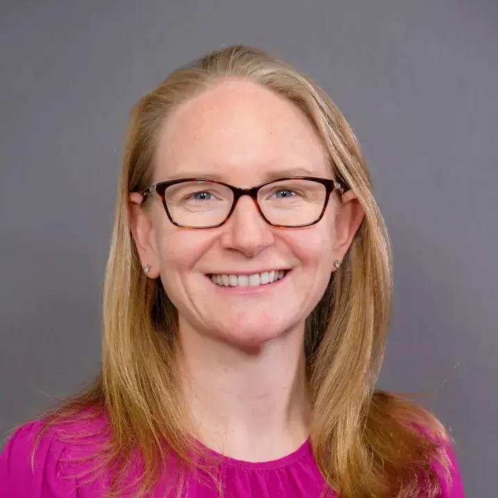 a person with long blonde hair and brown rimmed glasses wearing a bright pink blouse