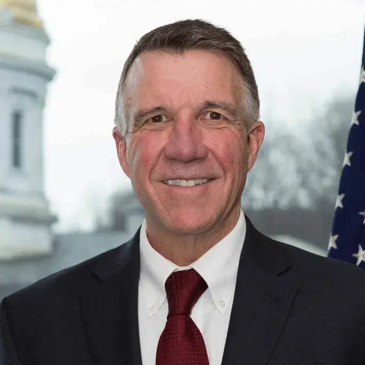 light skinned man smiling wearing dark jacket white shirt and maroon tie