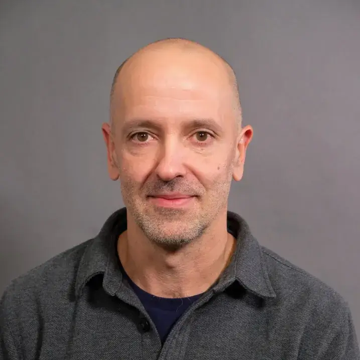 light skinned man with very short  hair wearing a black t-shirt and gray overshirtt