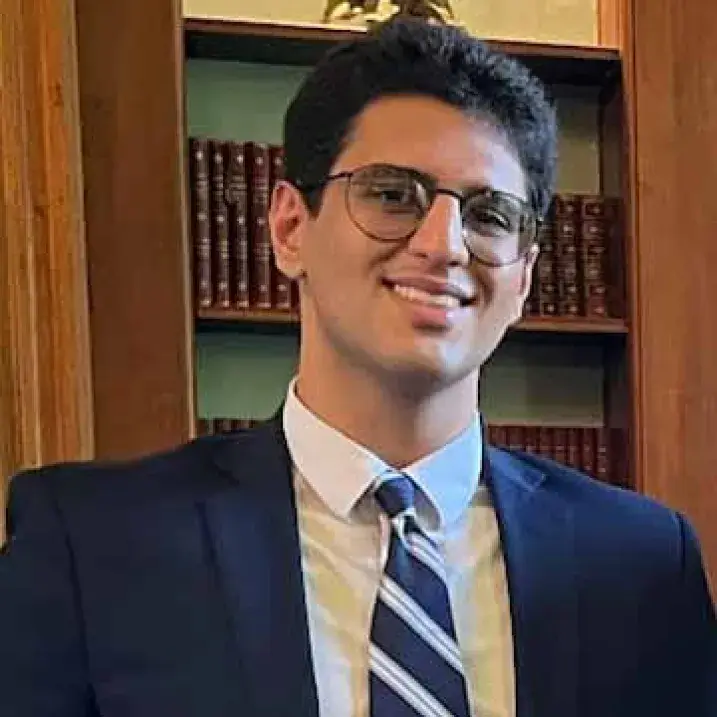 light skinned man with glasses and dark hair smiling wearing dark jacket and tie