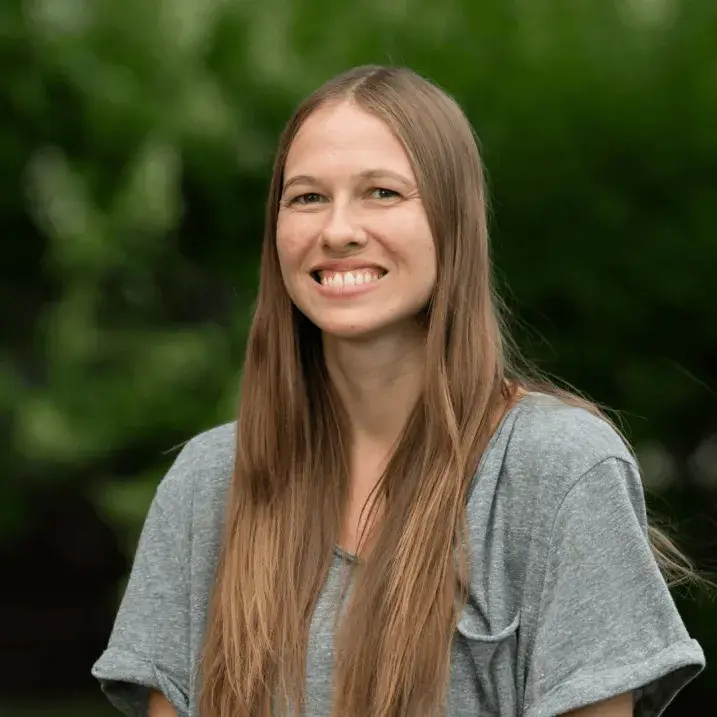 A photo of Colleen McGilpin, smiling and standing outside with a lush background.