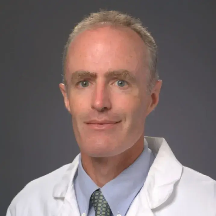 man with short gray hair wearing a blue shirt and doctors coat
