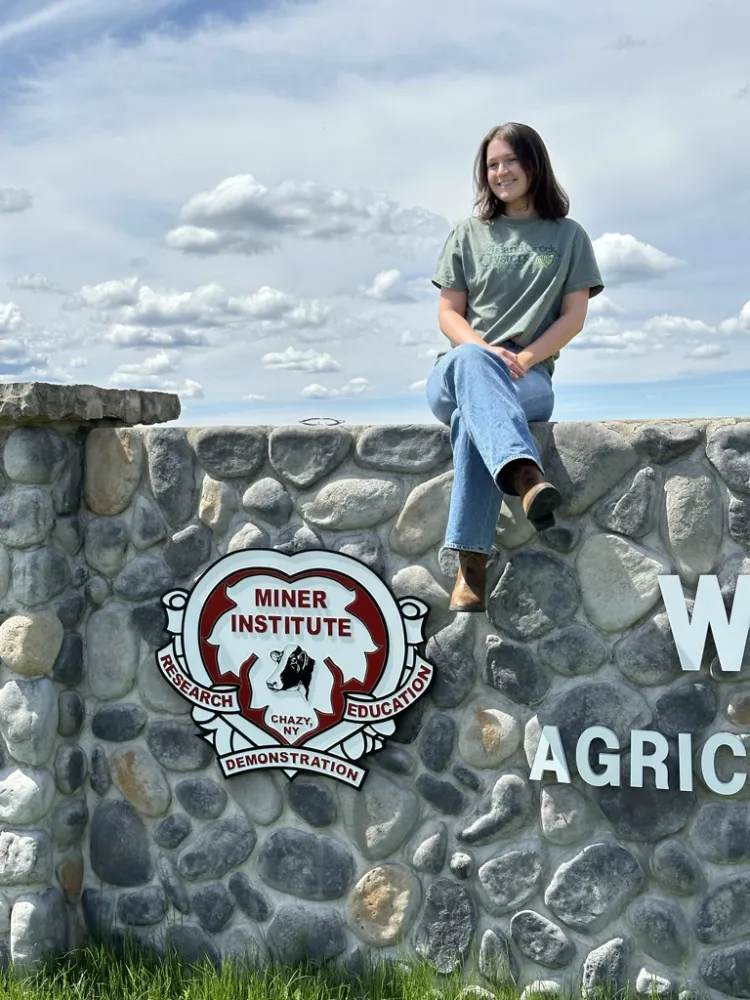 Girl sits on a stone wall that reads Miner Institute