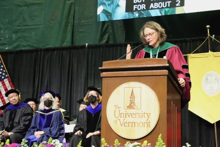 woman dressed in regalia giving commencement speech behind a UVM podium