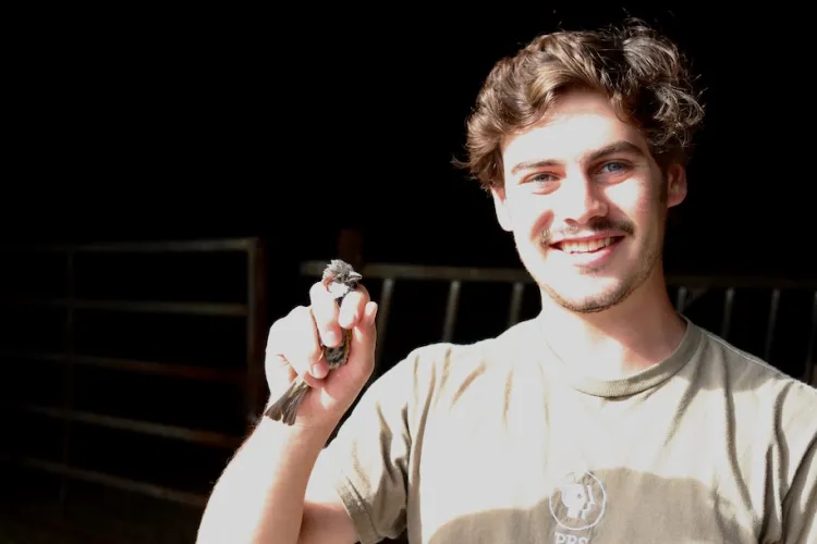 student holding a small bird in his hand and smiling at the camera.