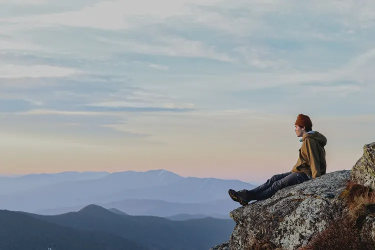 young man sitting on mountaintop with broad mountain vista