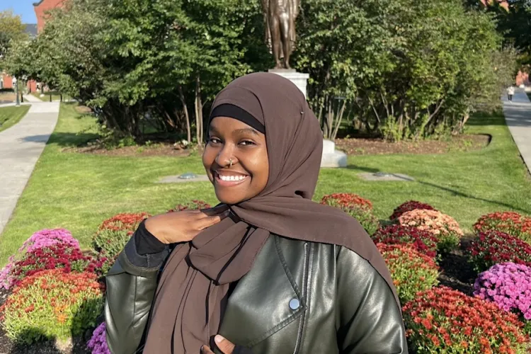 Halima Said smiling on campus in front of Ira Allen statue on the University Green.