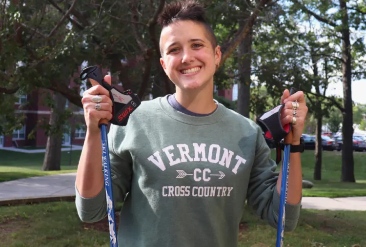 Riley Korhonen holding trekking poles with trees in background