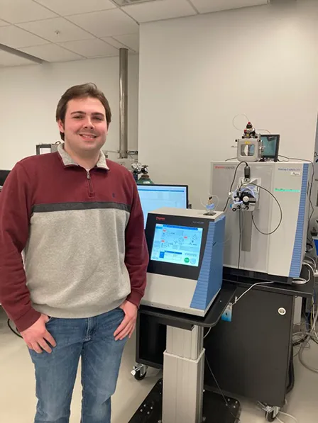 Brian Boyle standing in front of the mass spectrometer, where he analyzes data from samples.
