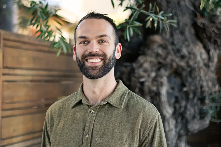 Young person smiling broadly indoor setting with large healthy plants in the background