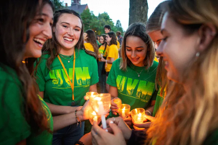 Five students huddle and smile around their candles as they light them.