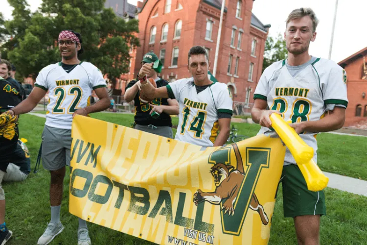 Three club football players in uniform hold a banner along a parade route.