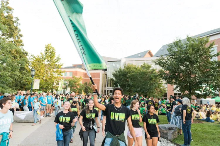 Student waves flag for sustainability Learning Community and guides a mass of students in parade.