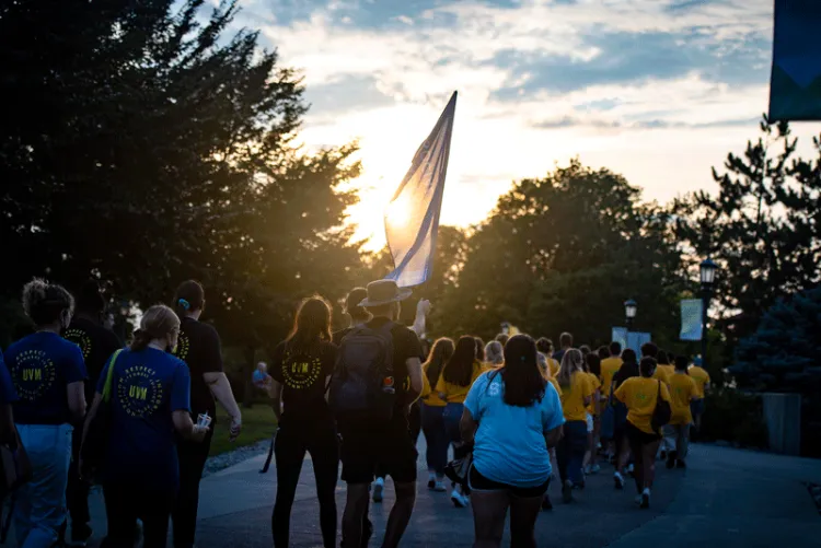 Students march to the Green while the sunsets into the treeline.