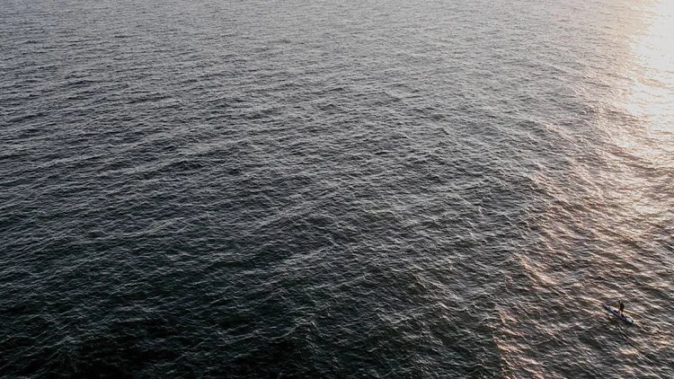 a small silouette of a man padding in a wide vast sea