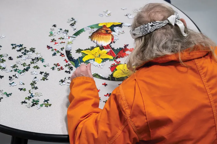an inmate wearing a bandana and orange jumpsuit works on a puzzle of flowers