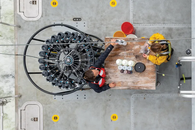 two people are photographed from above working at a wood table surrounded by scientific tools