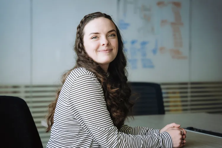 Bryn Loftness sits at a conference table. A flow chart appears in the background.