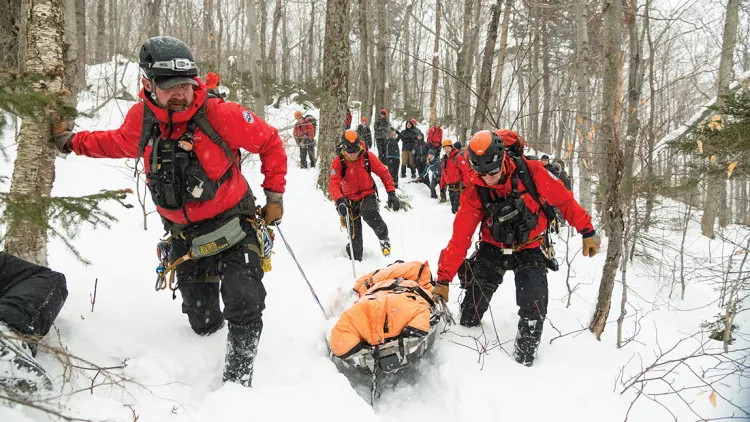 trainers drag a sled with a patient on it through the snow