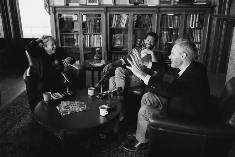 three professors sit around a coffee table chatting in a library