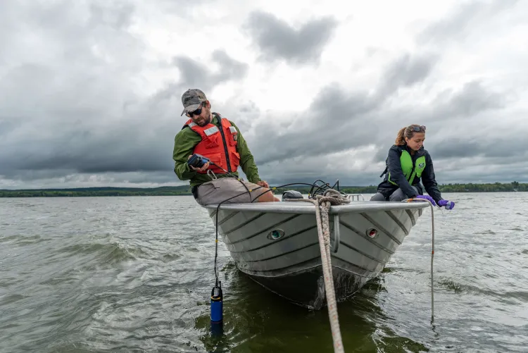 Two researchers in life jackets sit on the sides of a small motorboat on a lake.