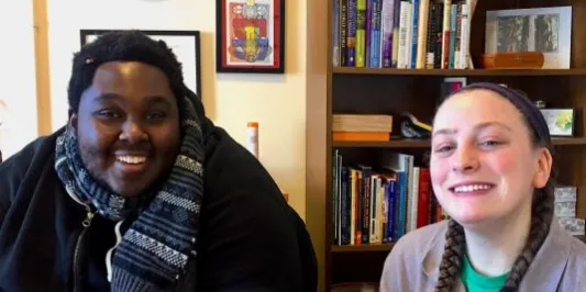 Two individuals seated in front of a bookcase, both smiling