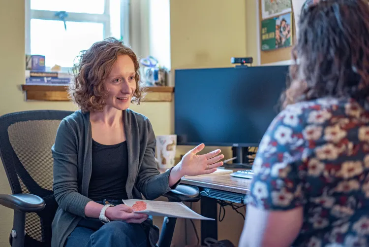 health and wellness coach mikaela young is talking with a student in her office and gesturing towards the student.