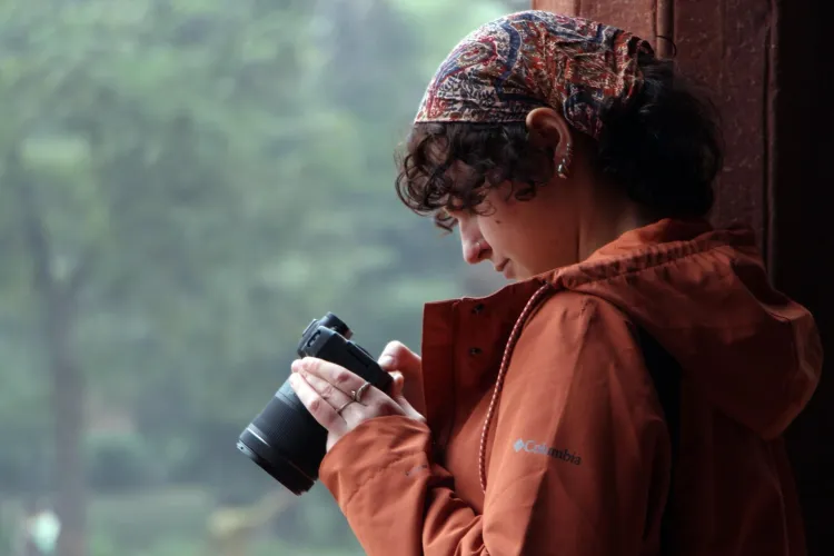 A student with a colorful bandana in her hair scrolls through preview of her photos on a DSLR camera.